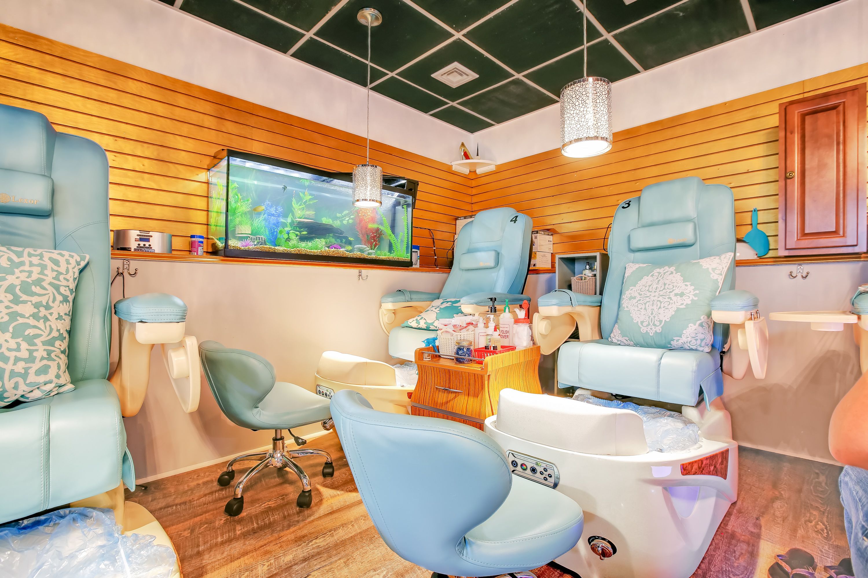 Un espace de bien-être moderne doté de deux fauteuils de massage, d’un grand aquarium et de panneaux muraux en bois.