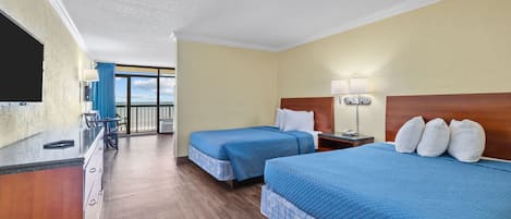 Ett hotellrum med två sängar, ett skrivbord, en stol, en TV och en balkong med utsikt.