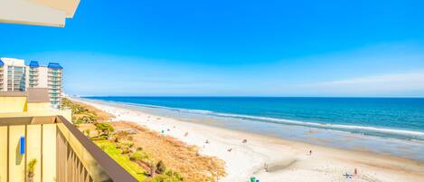 Uitzicht op een strand vanaf een balkon, met een zandstrand en een helderblauwe lucht.