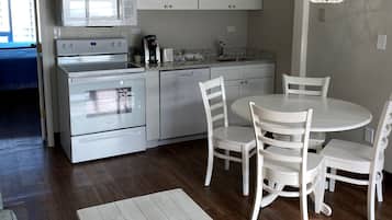 A modern kitchen with white cabinets, a built-in microwave, a stove, and a dishwasher. There is a dining table with white chairs and a hanging light fixture.