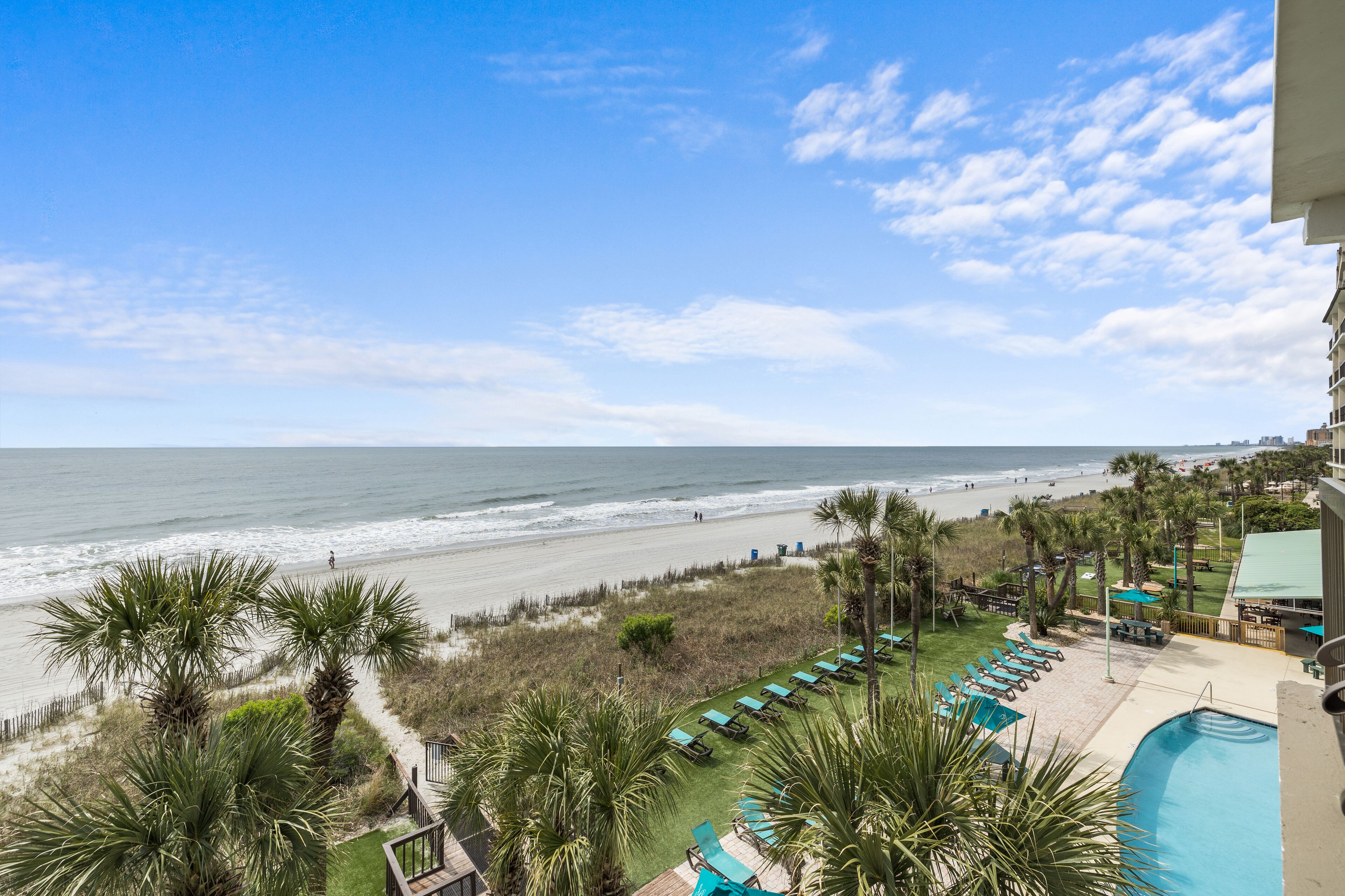A beachfront hotel with a pool, lounge chairs, and palm trees.