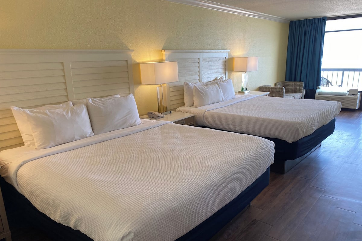Ein Hotelzimmer mit zwei Betten, Nachttischlampen, einem Nachttisch und einem Sessel, mit Blick ins Freie.