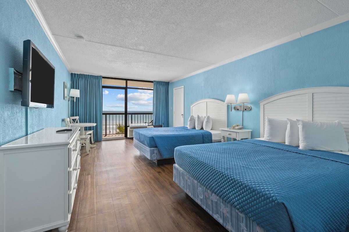 Ein Hotelzimmer mit zwei Betten, einem Fernseher, einem Schreibtisch und einem Balkon mit Blick.