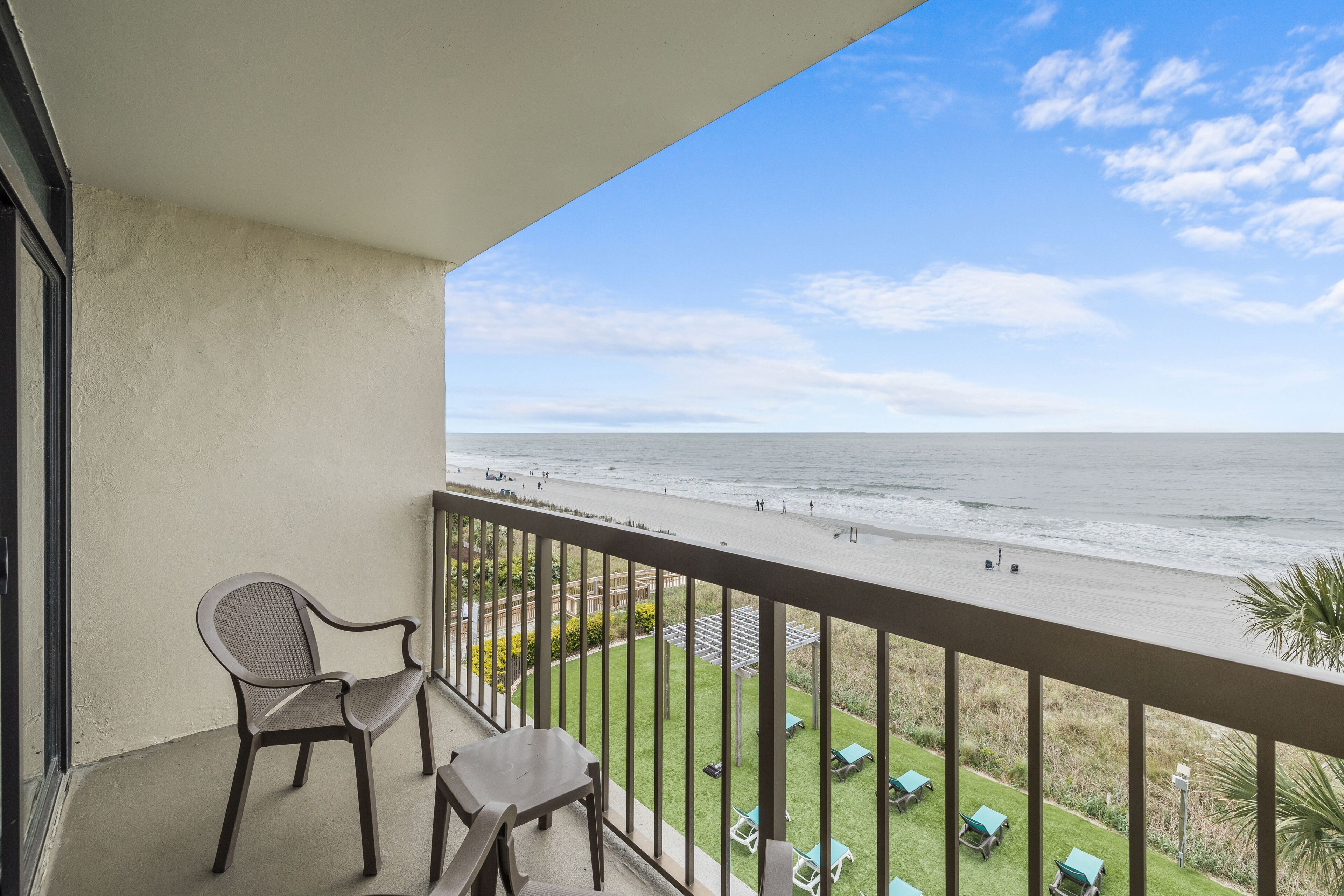 Un balcón con vista a la playa, una silla y una mesa.