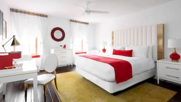 A modern bedroom with a large bed, white and red decor, a ceiling fan, and a wooden floor.