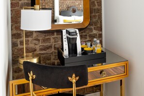 A hotel desk with a coffee maker, a lamp, and toiletries.