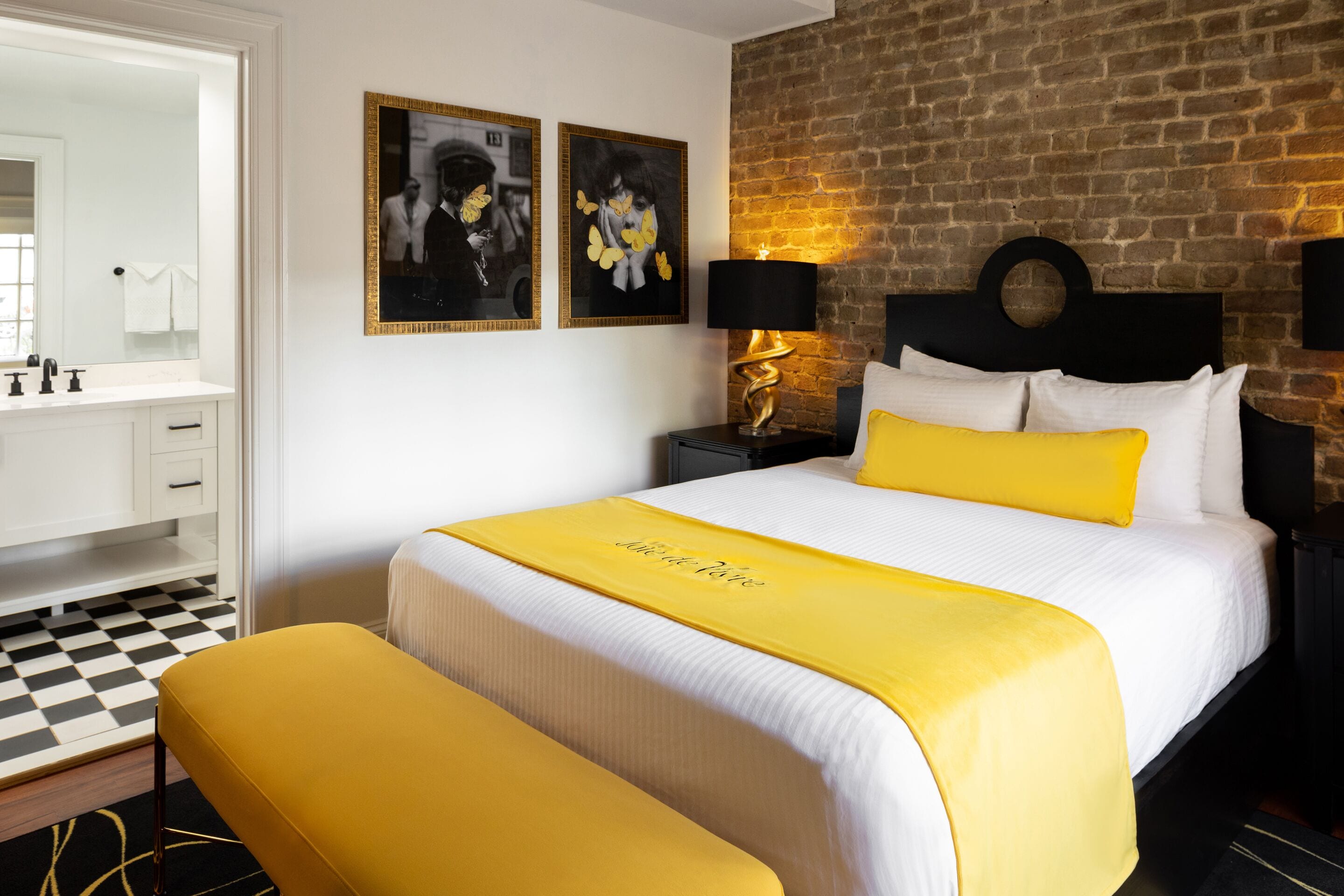 A hotel room with a bed, a nightstand, a lamp, a mirror, and a checkered floor.
