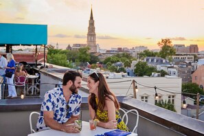 A couple dining at a rooftop restaurant with a city skyline and a church spire in the background. - The Vendue (Charleston)