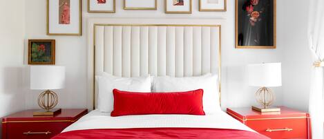 Une chambre d’hôtel avec un grand lit, une literie rouge, une tête de lit blanche et des œuvres d’art accrochées aux murs.