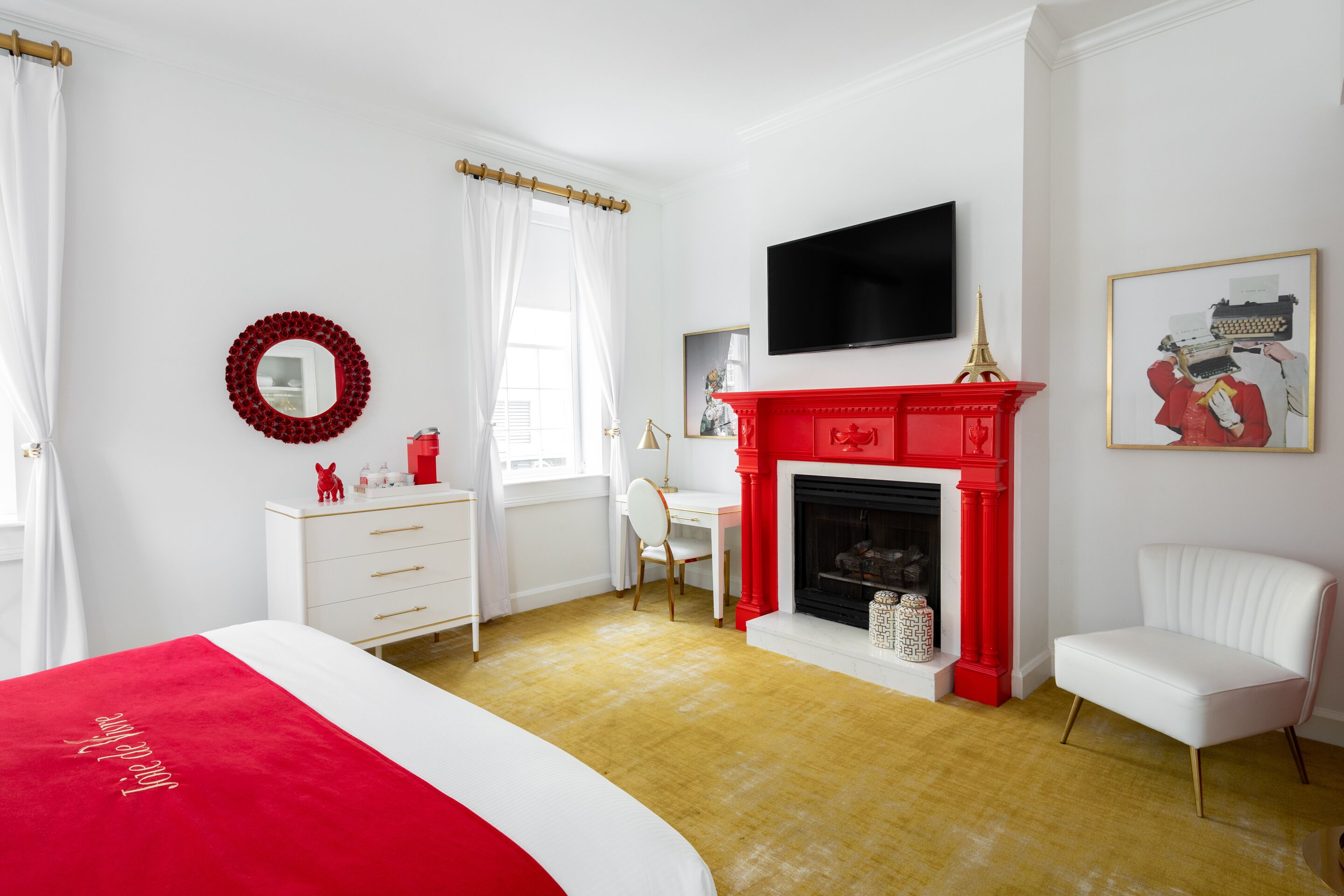 A bedroom with a bed, a desk, a chair, a fireplace, and a TV.
