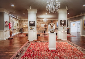 Enter a grand lobby with a high ceiling, adorned with sculptures and artworks, and a door leading to more.