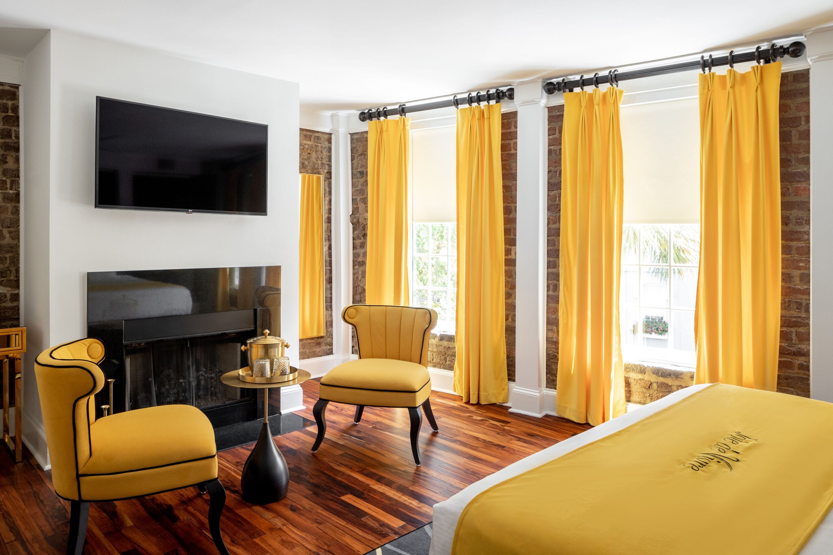 Une chambre d’hôtel avec une cheminée, un téléviseur fixé au mur, deux fauteuils jaunes et un lit recouvert d’une couverture jaune.