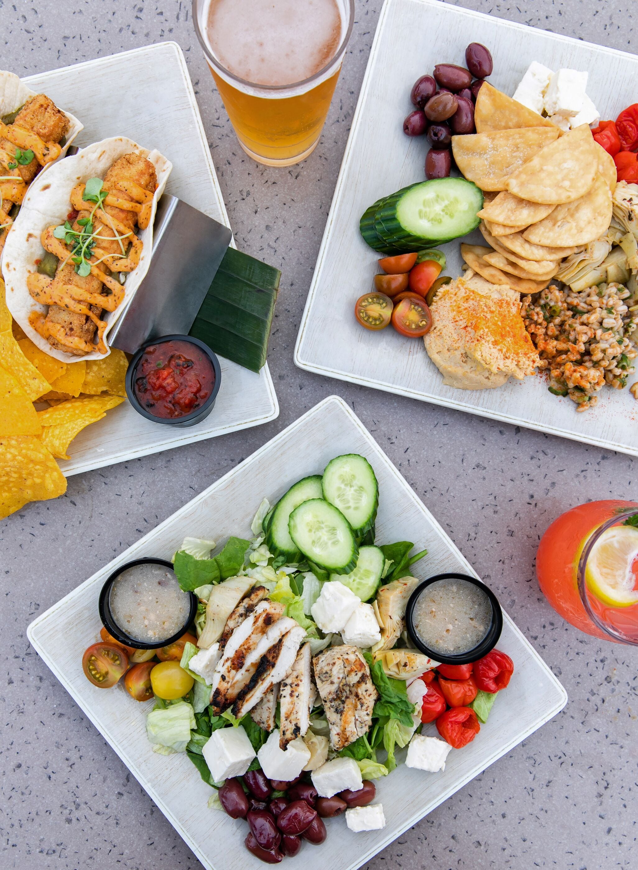 A table with various dishes including tacos, a salad, and a drink.