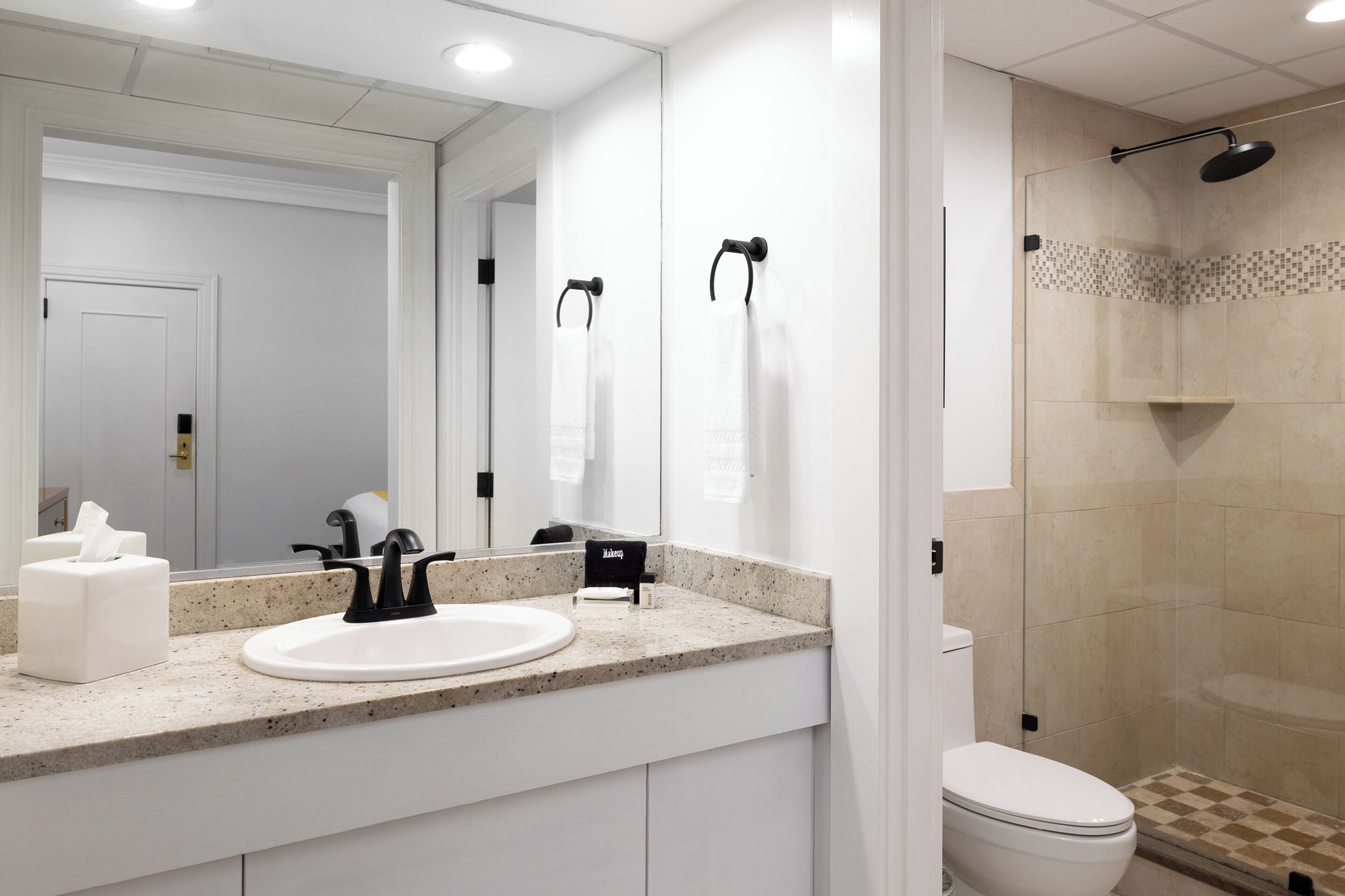 Un baño moderno con lavamanos blanco, grifo negro y ducha con mampara de vidrio.