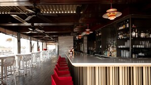 Zona de bar con una barra alargada, taburetes rojos y una variedad de botellas en estantes.