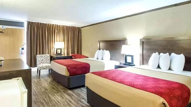 Habitación de hotel con dos camas, un escritorio, una silla y una lámpara.