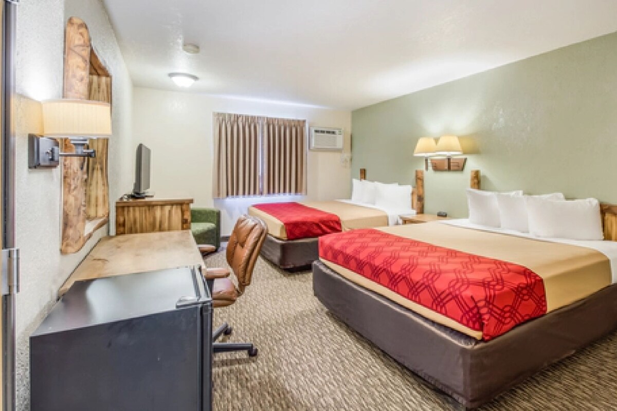 A hotel room with two beds, a desk, a chair, and a television.