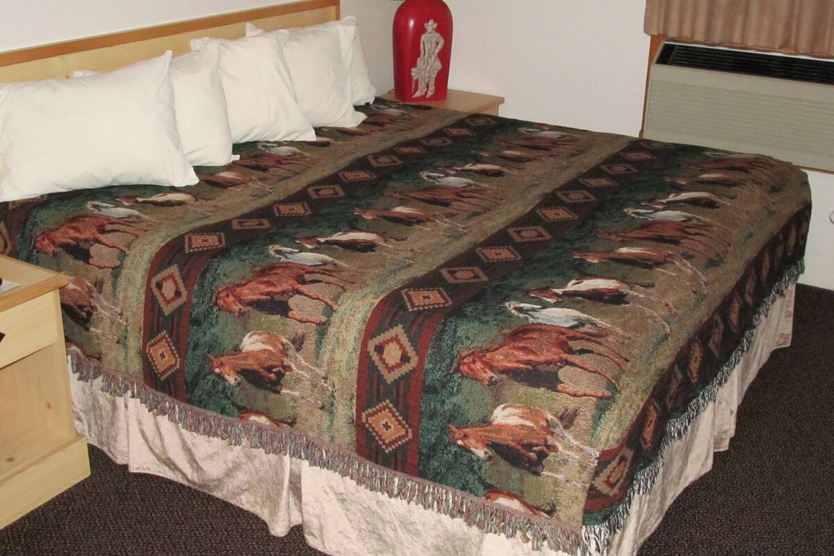 Habitación de hotel con cama, mesita de noche con lámpara y control remoto, un jarrón rojo y una colcha estampada.