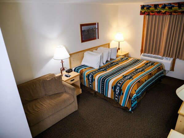 A hotel room with a bed, a bedside table with a lamp, a couch, and a window with curtains.