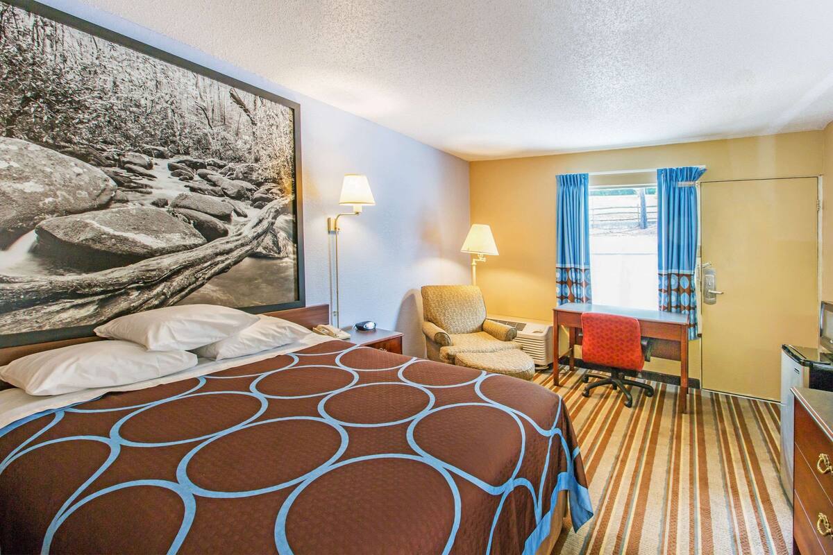 Une chambre d’hôtel avec un grand lit, un bureau, une chaise et une fenêtre avec des rideaux.
