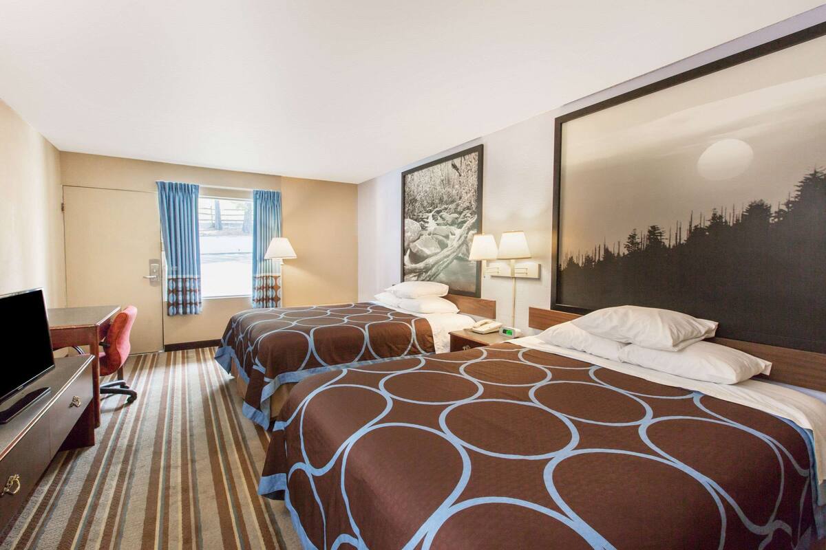 Une chambre d’hôtel avec deux lits, un bureau, une télévision et une fenêtre avec des rideaux.