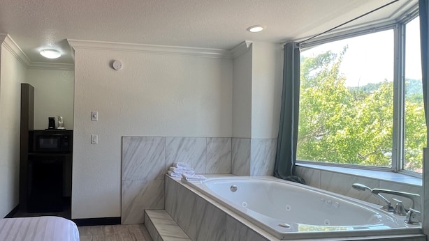 A modern bathroom with a large bathtub, a shower area, and a window providing a view of greenery. - Reagan Resorts Inn (Gatlinburg)