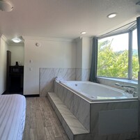 A modern bathroom with a large bathtub, a shower area, and a window providing a view of greenery.