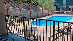 A swimming pool with a stone wall and metal fence, surrounded by a patio area with outdoor furniture. - Reagan Resorts Inn (Gatlinburg)