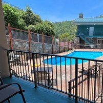 A swimming pool with a stone wall and metal fence, surrounded by a patio area with outdoor furniture.