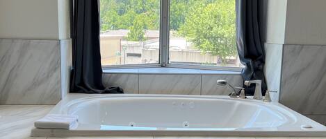 Un baño con una bañera grande, una ventana con cortinas y baldosas de mármol.