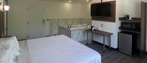 Una habitación de hotel con cama, un escritorio pequeño, microondas, refrigerador, ducha y televisor.