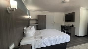 Una habitación de hotel con una cama grande, un escritorio con silla, un televisor montado en la pared y un armario.