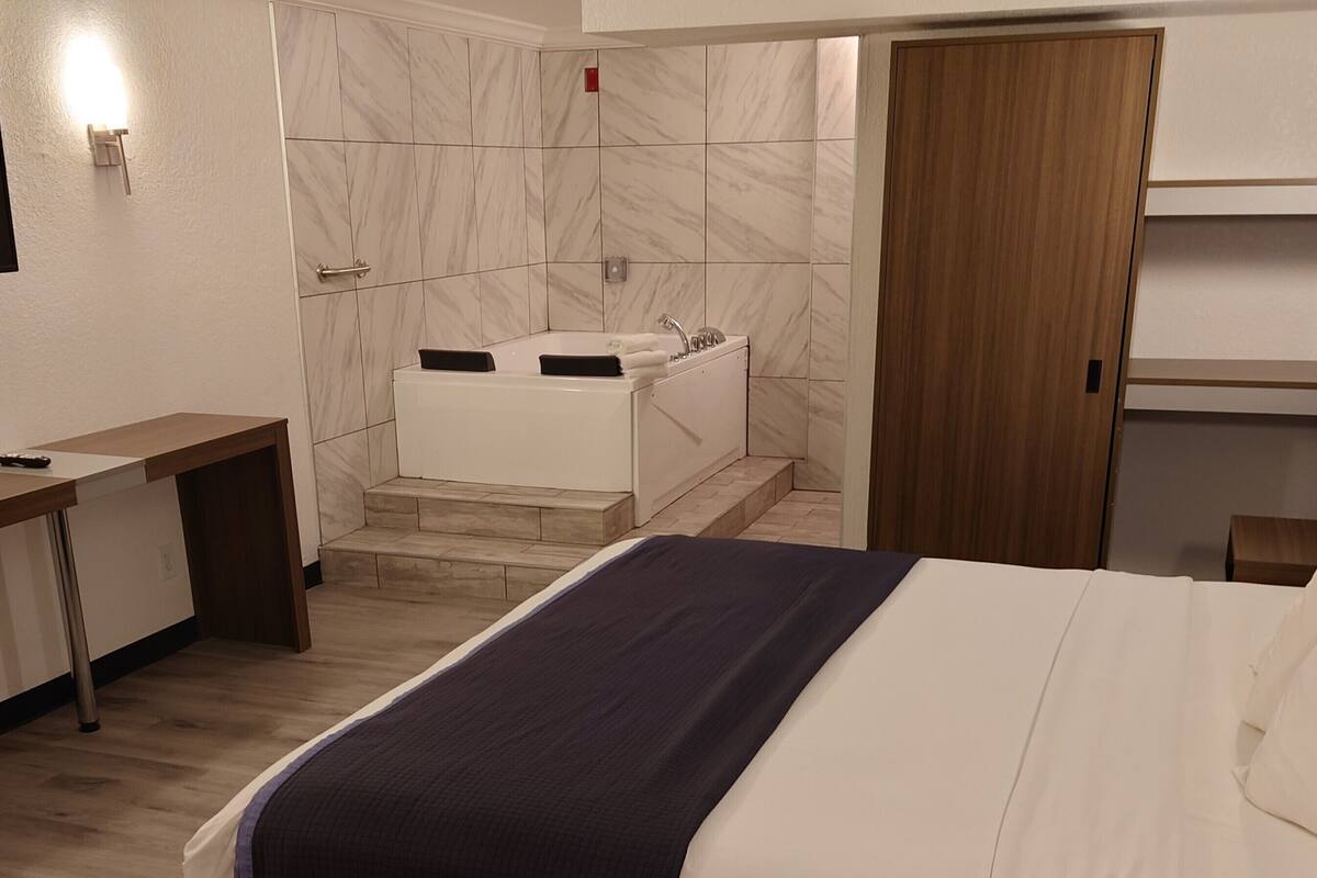Une chambre d’hôtel comprenant un lit, un bureau, une salle de bain avec baignoire et une armoire.