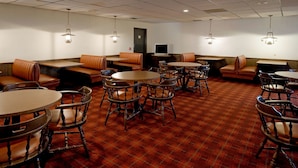 Un hall d’hôtel doté de plusieurs espaces aménagés avec des sièges, notamment des banquettes et des tables rondes, ainsi qu’un téléviseur posé sur un meuble.