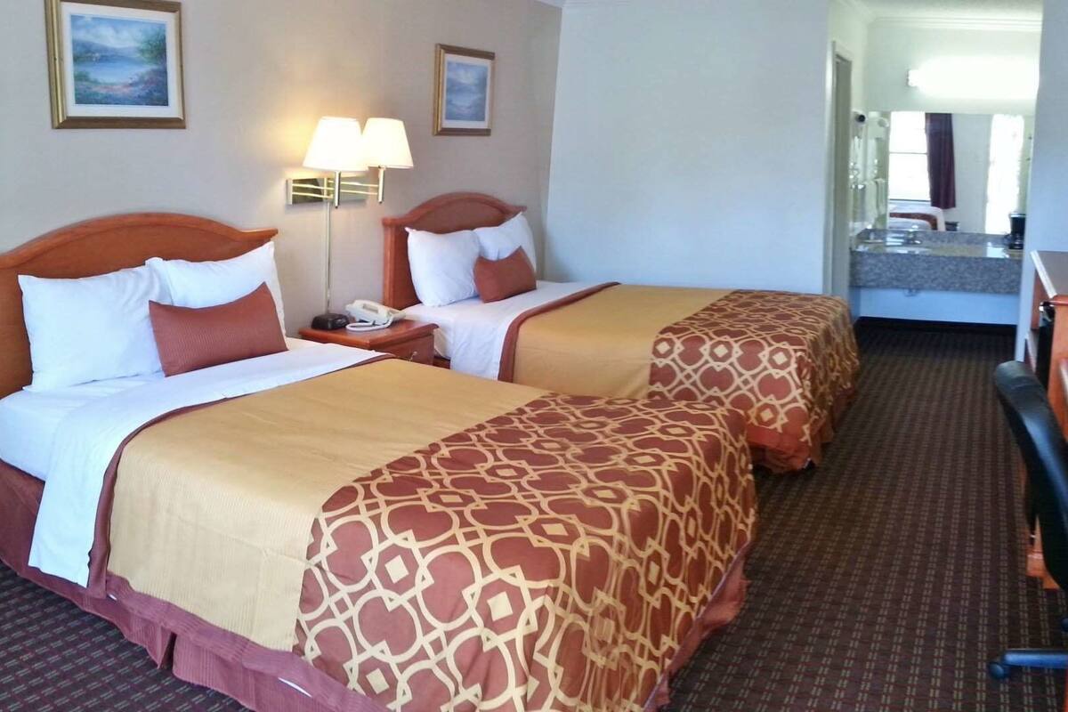 A hotel room with two beds, a desk with a computer, a TV, and a mirror.