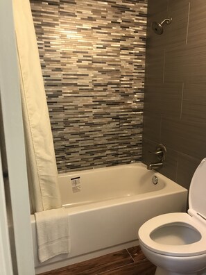A bathroom with a tiled shower wall, a bathtub, and a toilet.