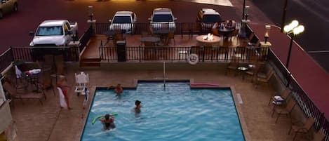 Un área de piscina en la azotea con piscina, sillas de descanso y mesas.