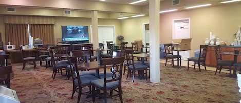 A conference room with multiple tables and chairs, a television, and a door.
