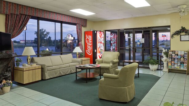Um lobby de hotel com um sofá, poltronas, uma mesa de centro, uma televisão e uma máquina de venda automática de Coca-Cola.