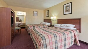 Quarto de hotel com duas camas, uma mesa com cadeira, televisão e banheiro ao fundo.