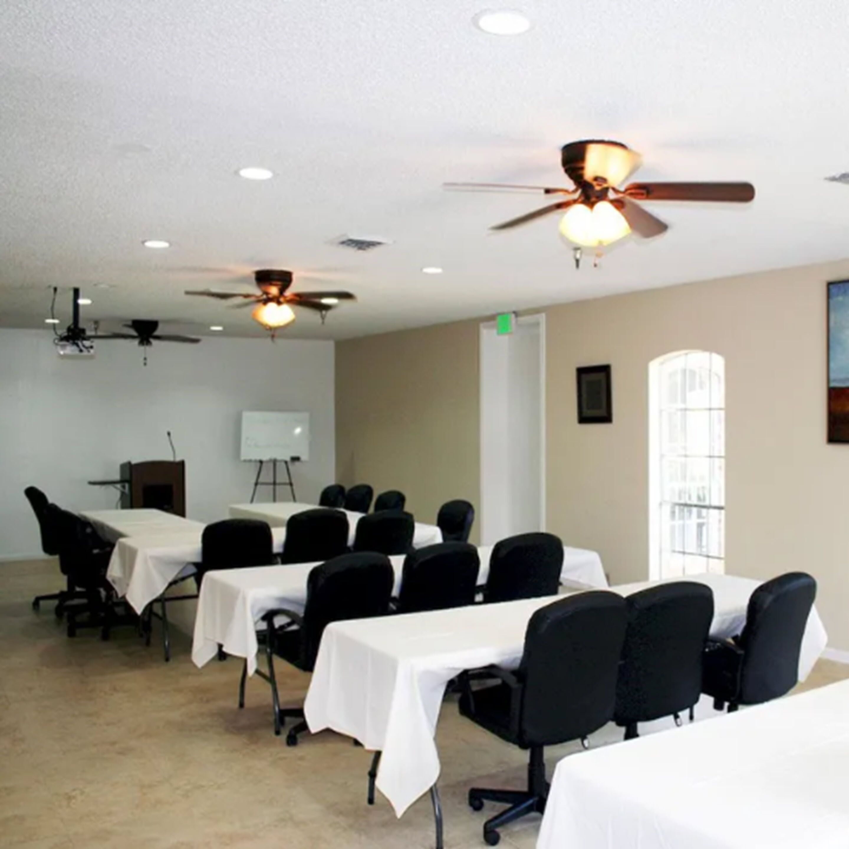 A conference room with multiple tables and chairs, ceiling fans, and a whiteboard.