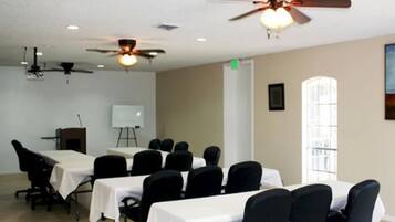 A conference room with multiple tables and chairs, ceiling fans, and a whiteboard.