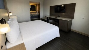 Ein Hotelzimmer mit Bett, Nachttischlampe, Schreibtisch, Stuhl und einem wandmontierten Flachbildfernseher.