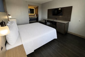 Habitación de hotel con cama, lámpara de noche, escritorio, silla y televisor de pantalla plana montado en la pared.