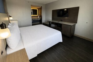 Habitación de hotel con cama, lámpara de noche, escritorio, silla y televisor de pantalla plana montado en la pared.