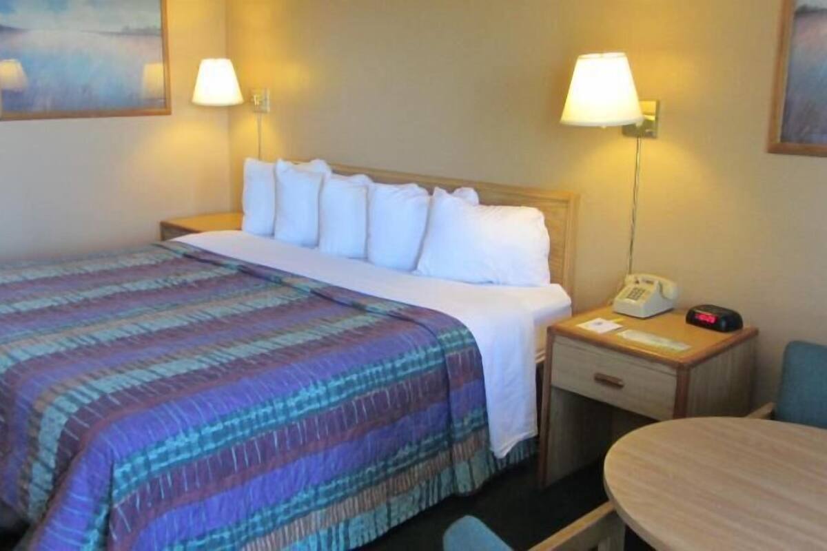 Habitación de hotel con cama, lámparas de noche, teléfono en la mesita de noche, una silla y una mesa.