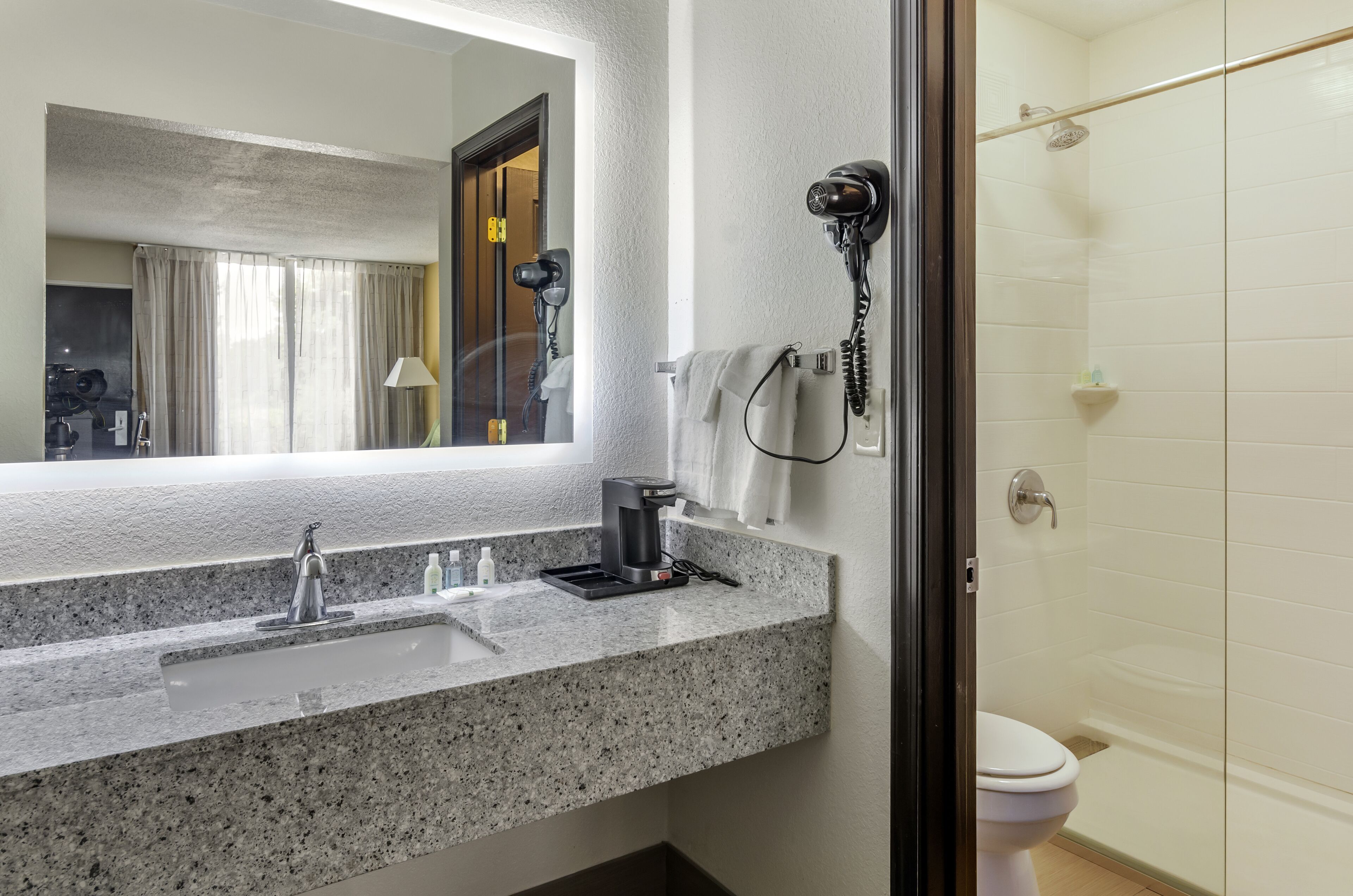 Baño con encimera de granito, lavamanos, secador de pelo y ducha.