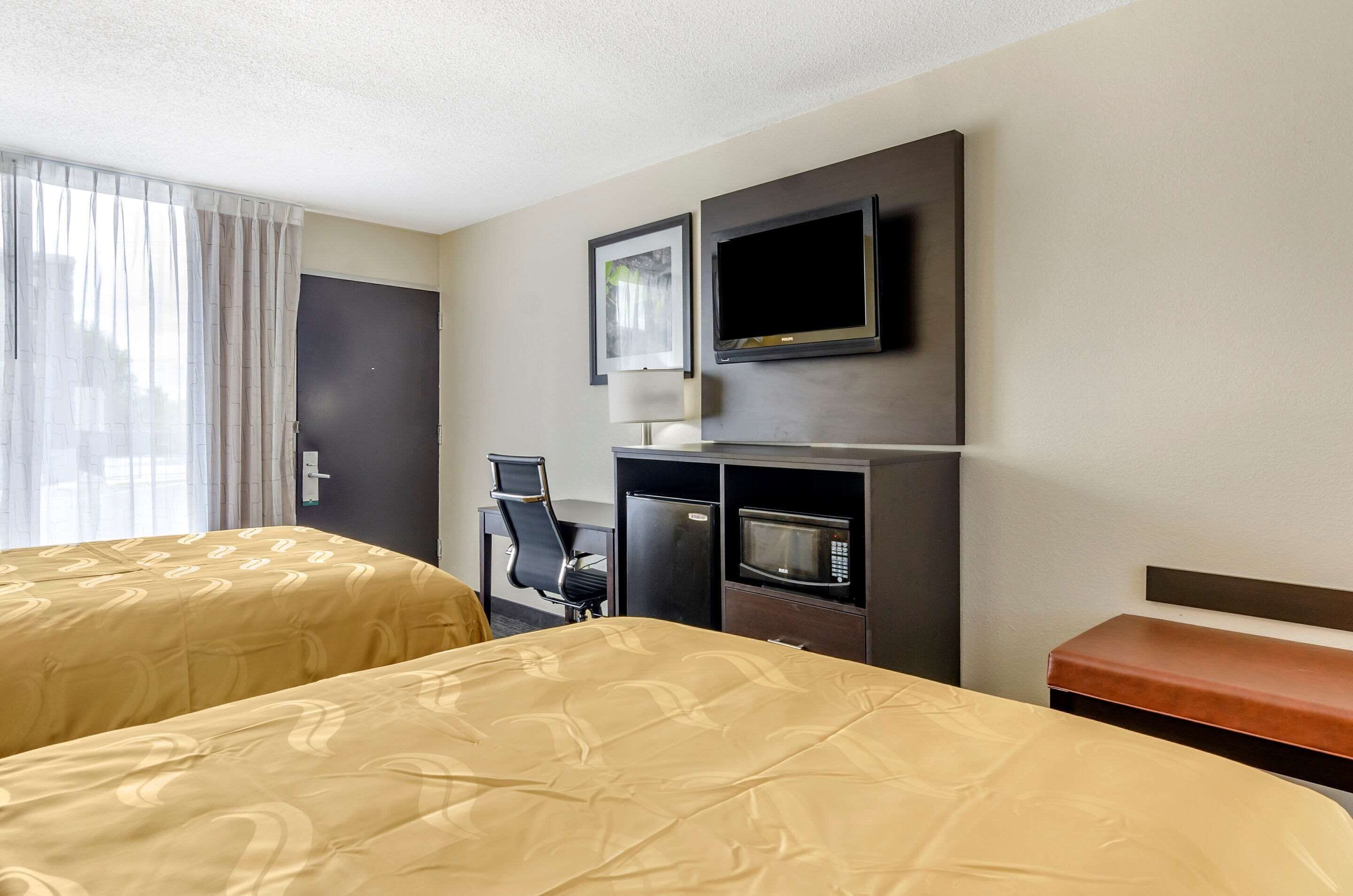 Habitación de hotel con dos camas, un escritorio con silla, televisor y microondas.