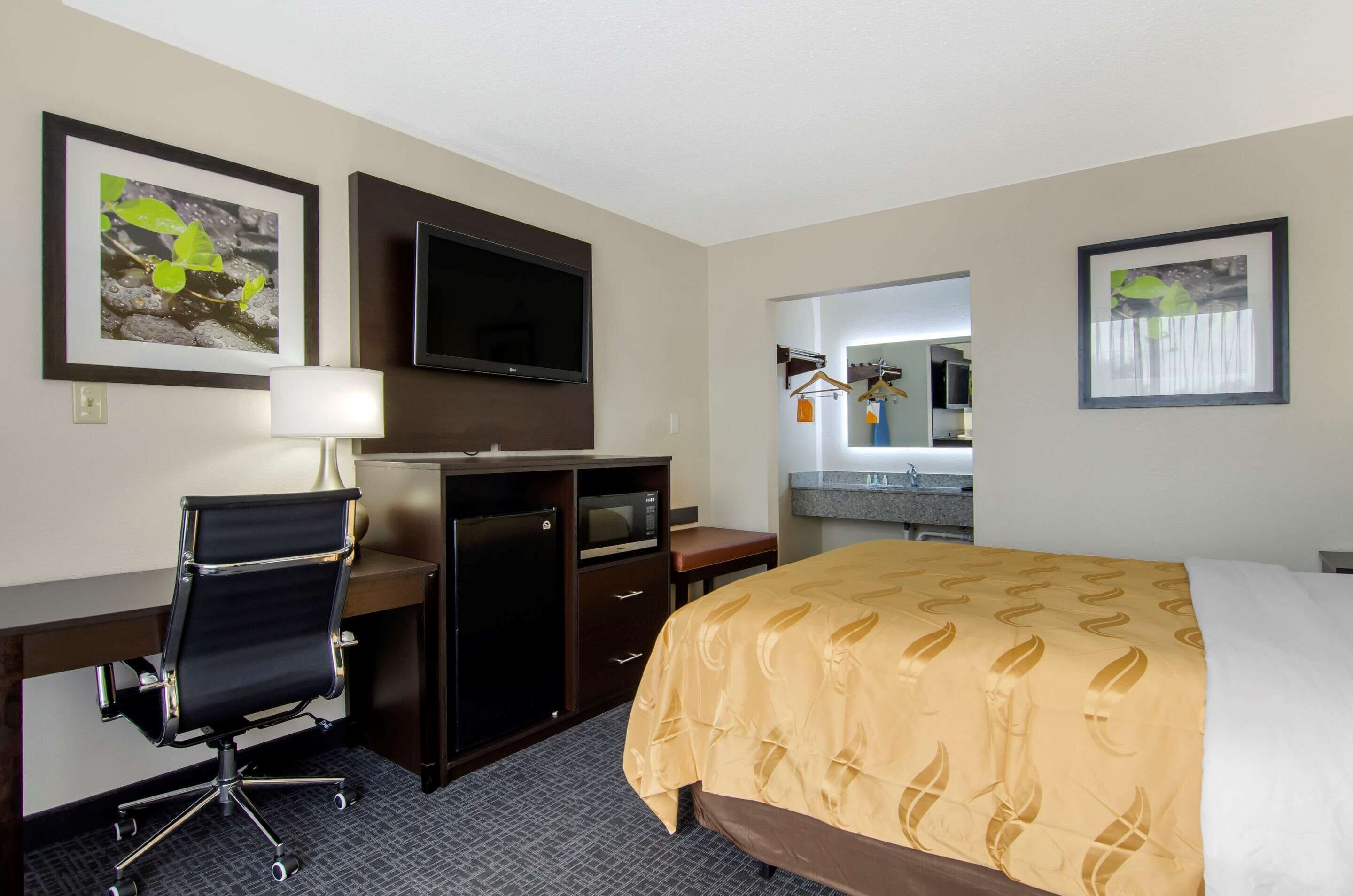 A hotel room with a desk, chair, television, bed, and artwork on the walls.
