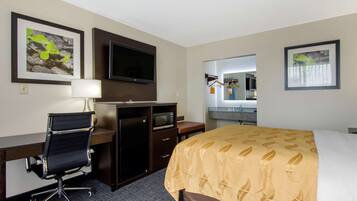 A hotel room with a desk, chair, television, bed, and artwork on the walls.